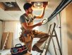 electrician-installing-recessed-lighting A skilled electrician installing recessed lighting in a residential home, standing on a ladder with tools and exposed wiring, demonstrating precision and expertise in electrical installations.